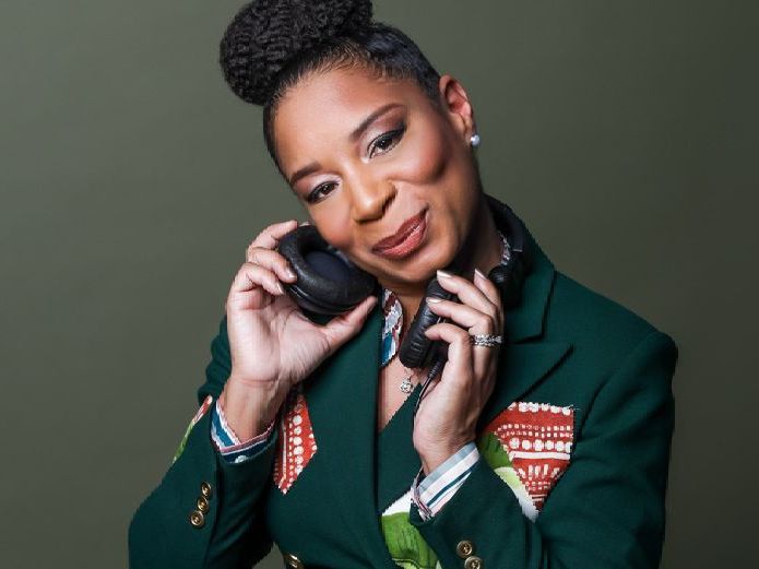 a woman in a green jacket is holding a pair of headphones .